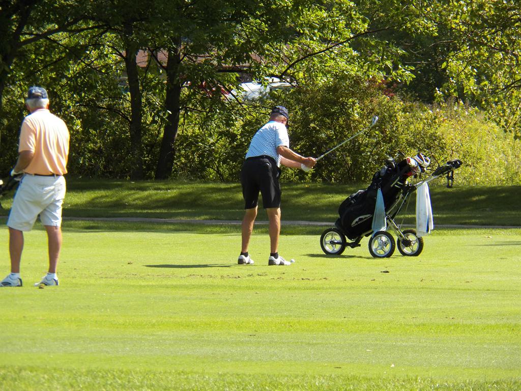 Ron Marande starts his backswing on his approach shot on #12 with Don Walsh lookiing on.